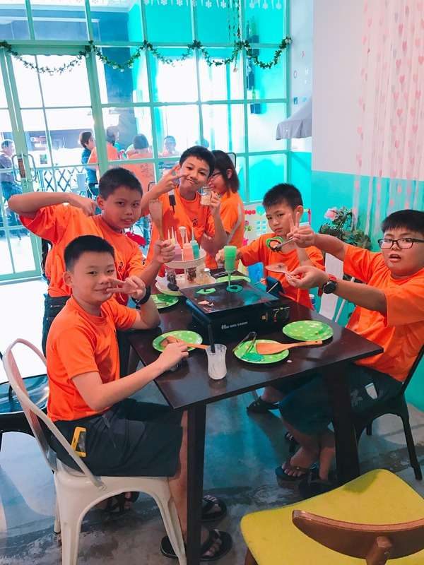 School outing participants in orange team shirts making DIY pancakes at a table